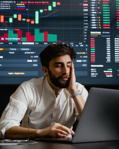Male data specialist analyzing economic statistics on computer screens
